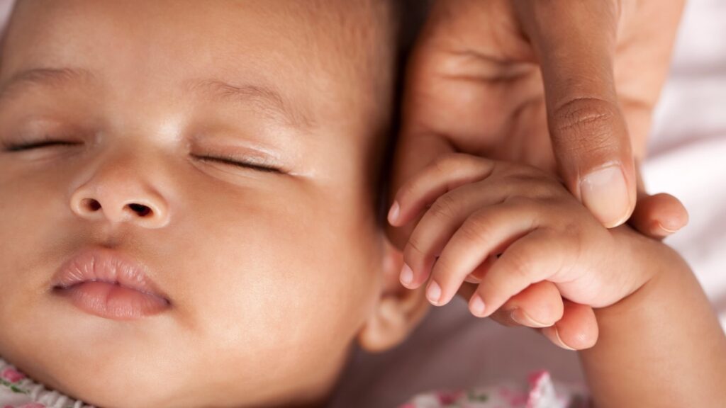 close up of baby sleeping while holding parent's hand