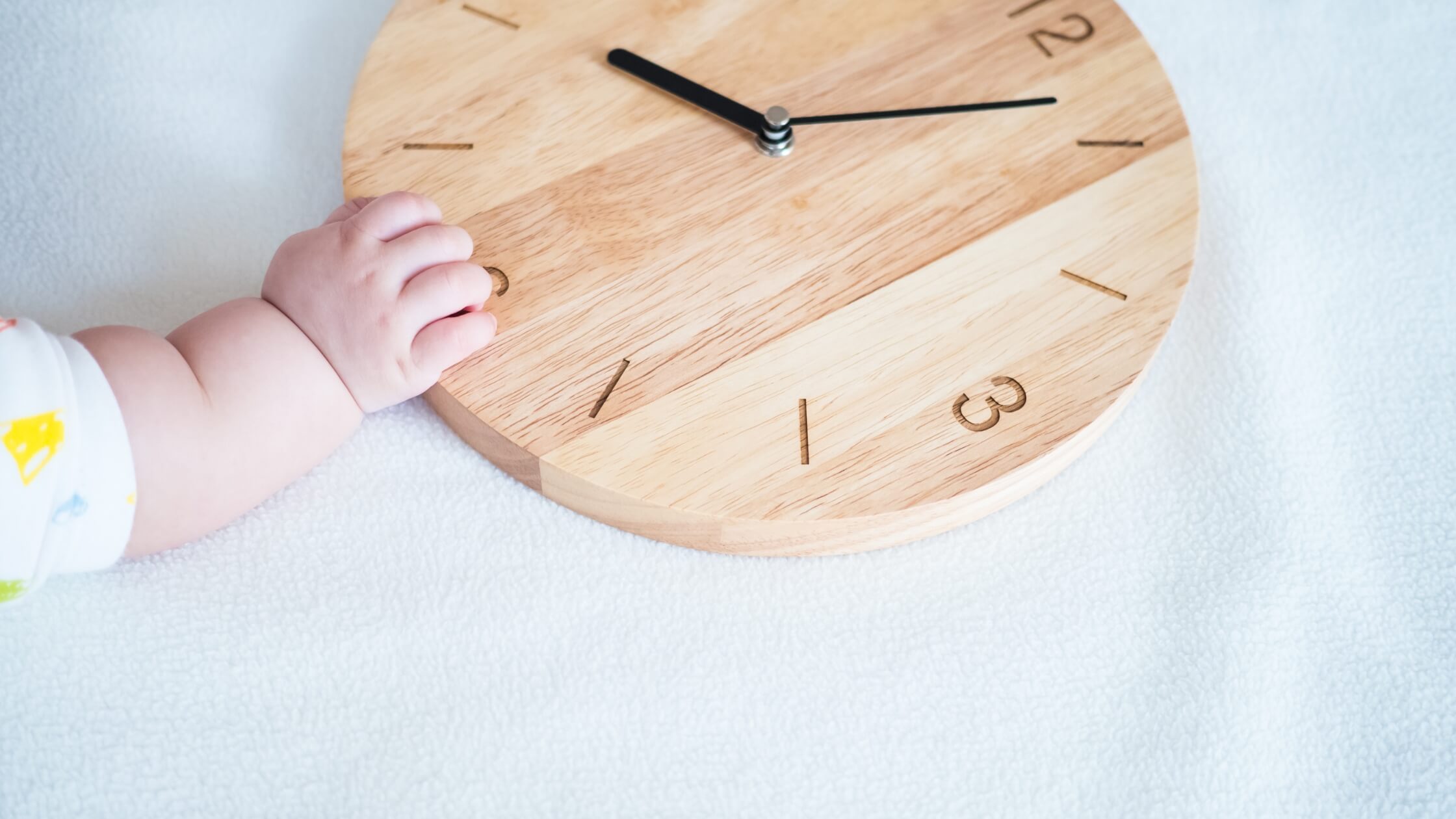 baby in crib with its hand on a clock