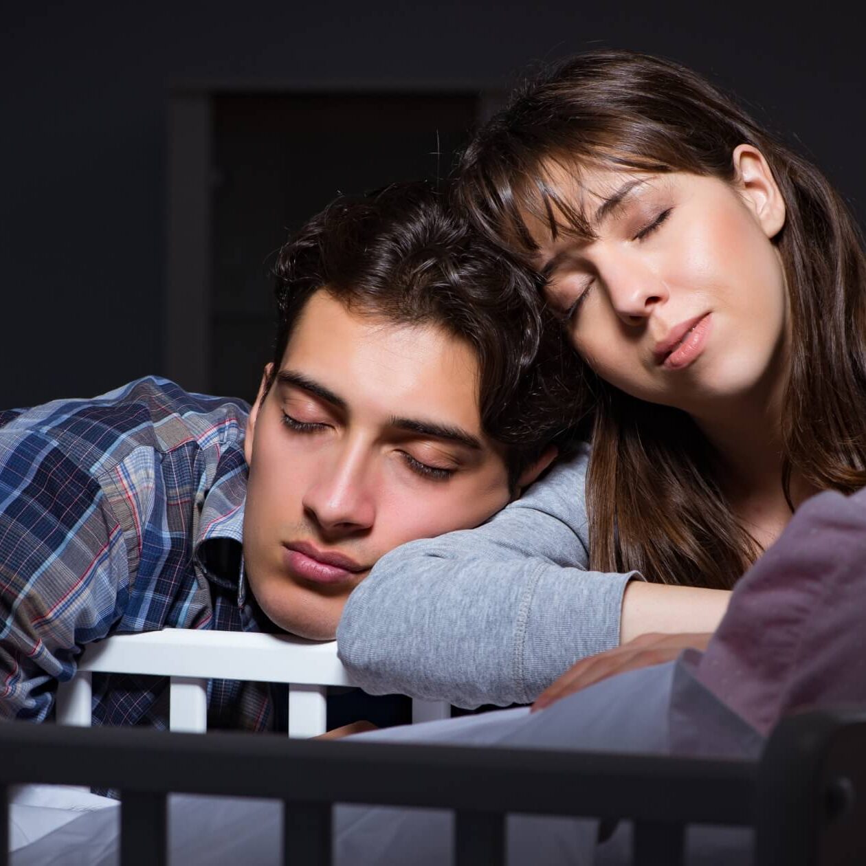 parents falling asleep over a crib at night